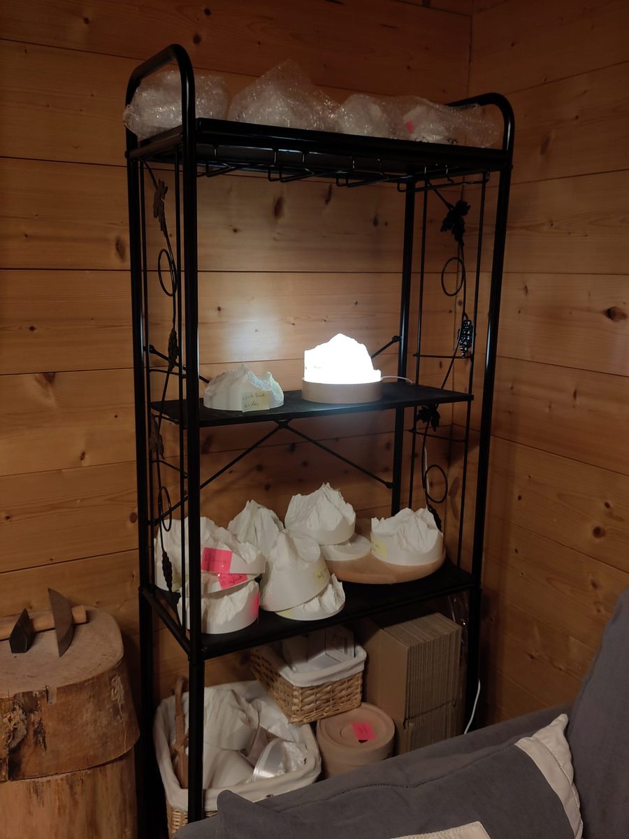 Étagère de l'atelier avec les lampes de montagne en stock, une lampe allumée sur son socle en poirier